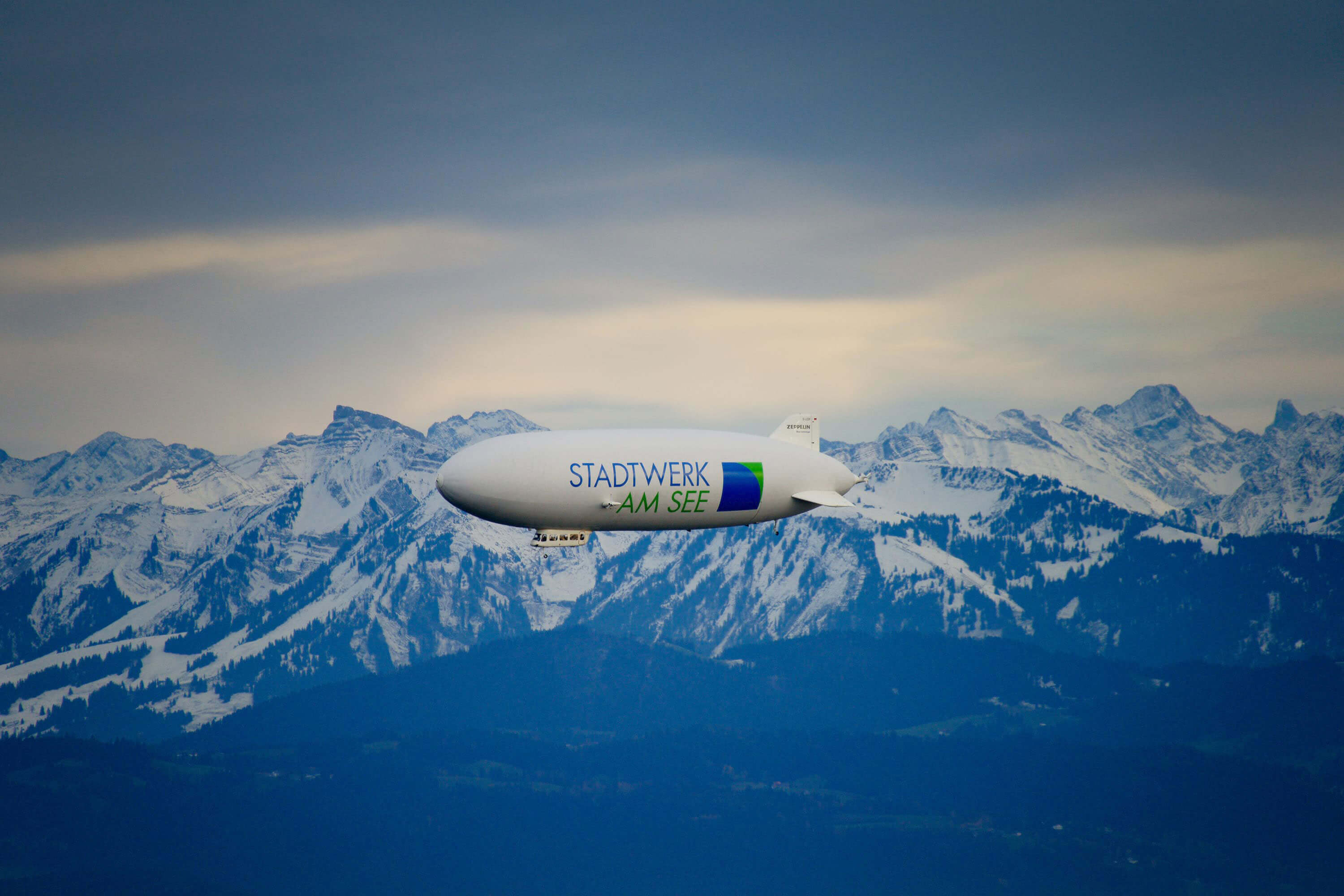 Zeppelin mit Logo Stadtwerk am See in den verschneiten Bergen