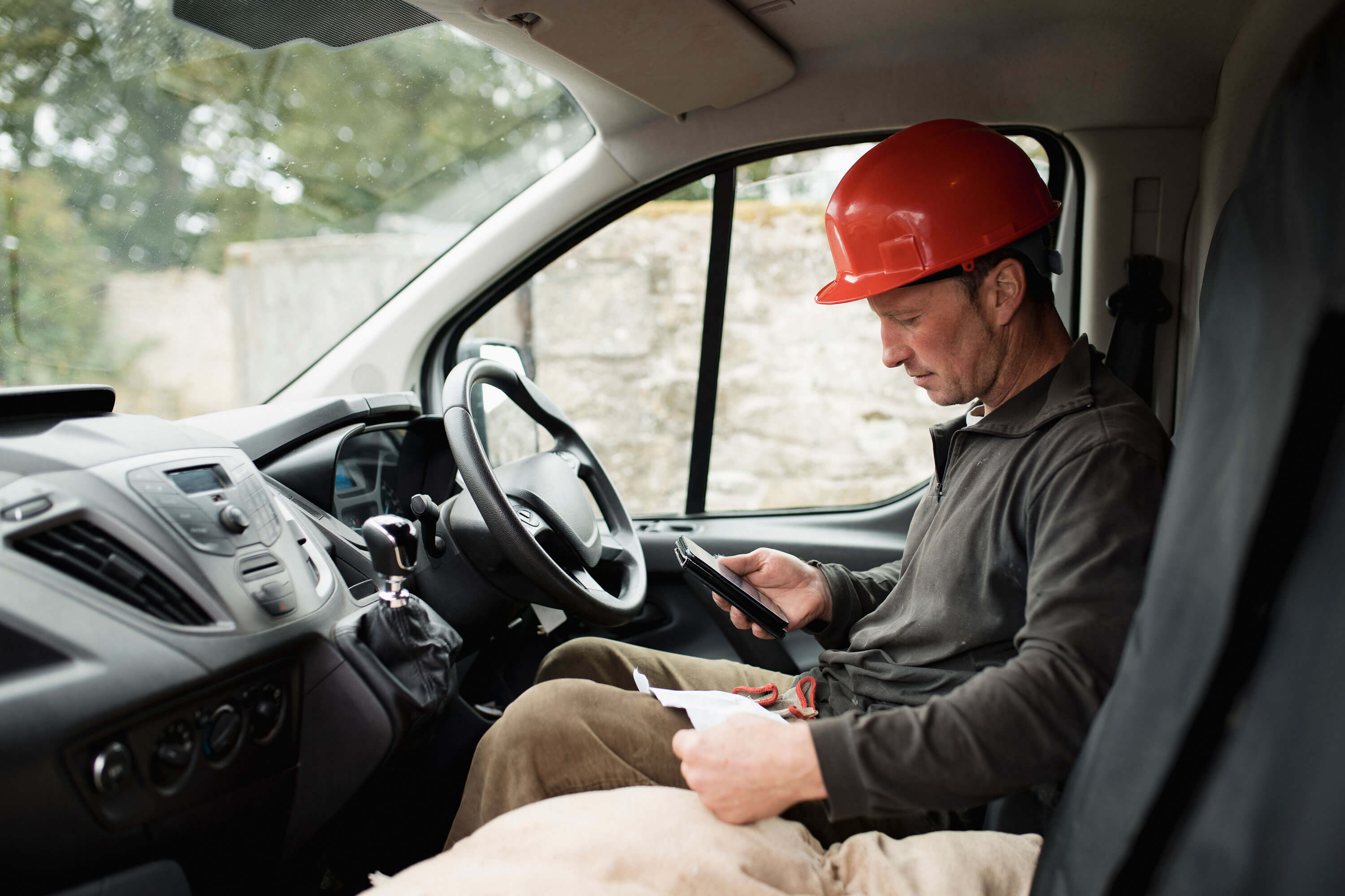 Mann mit Helm sitzt im Auto und schaut Rechnung an