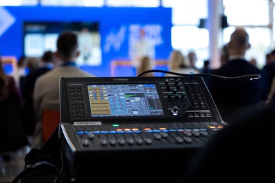 Hintergrundtechnik bei einer Veranstaltung mit Bühne. Dabei ist der Hintergrund mit der Bühne unscharf zu sehen und die Technik im Vordergrund scharf.