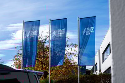 3 blaue Fahnen im Außenbereich eines Gebäudes mit einem Logo und dem Schriftzug 