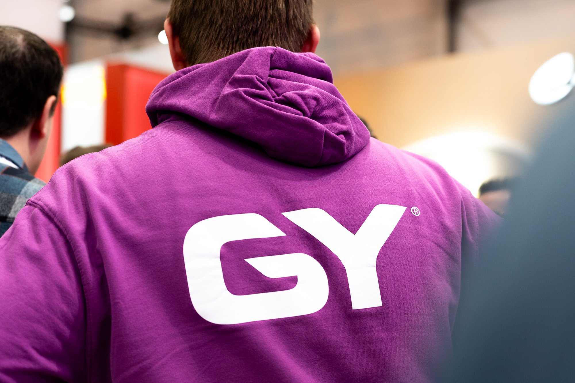 Mann trägt einen lila GY Hoodie, das Logo ist weiß und hinten unter der Kaputze auf dem Rücken sichtbar.