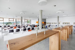 Großer heller Raum mit Tischreihen und Stühlen und vielen bodentiefen Fenstern